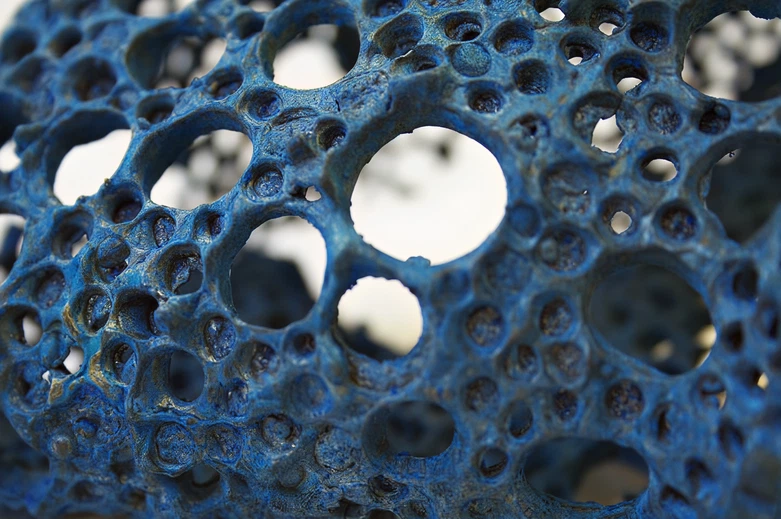 A closeup of a bronze sculpture I made based on organic, coral-like forms with a pattern of circular holes, treated with a blue patina